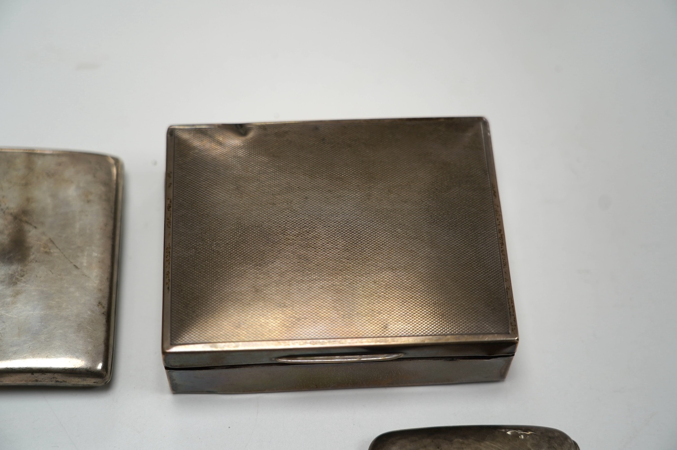 A George VI part engine turned silver mounted cigarette box, by Mappin & Webb, Birmingham, 1937, 11.5cm, together with another silver mounted cigarette box by Garrard & Co and four assorted silver cigarette cases. Condit